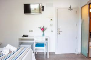 Innenansicht eines Hotelzimmers von Rosales Formentera mit Bett, Schreibtisch und Fernseher an der Wand.