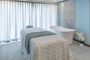 Massageraum im Sands Barbados mit Behandlungsliege, Badewanne und weißen Vorhängen.