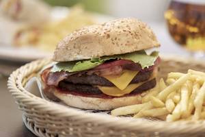 Ein Burger mit Pommes in einem Korb auf einem Tisch neben einem Glas Bier.