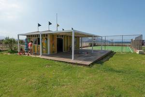 Außenansicht des Eliros Mare Hotel mit einem bunten Kinderspielhaus auf einem Sportplatz.