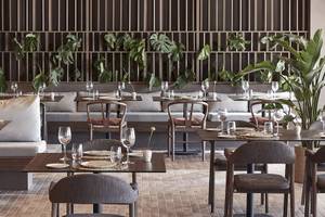 Innenansicht des Restaurants im Helea Lifestyle Beach Resort mit gedeckten Tischen und grünen Pflanzen.