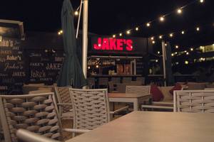 Nachtansicht der Terrasse von Jake's im Coconut Court Beach Hotel mit leuchtenden Lichtern und Tischen.
