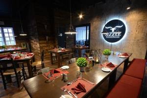Inneneinrichtung des Sizzle Steakhouse mit langen Holztischen, roten Sitzbänken und grün dekorierten Tischen.