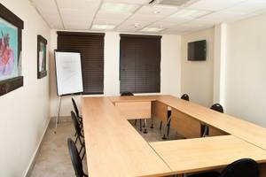 Konferenzraum im Rostrevor Hotel mit langen Holztischen, schwarzen Stühlen, einer Tafel und einer Fernsehwand.