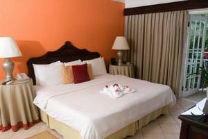 Schlafzimmer im Mango Bay Hotel mit zwei Nachttischen, Lampen und einem großen Bett, das mit weißen Laken und bunten Kissen ausgestattet ist.