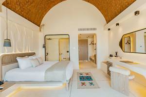 Innenansicht eines eleganten Zimmers im Sunrise Anjum Resort mit einem großen Bett, weißen Wänden und einem großen Spiegel.