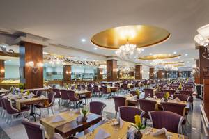 Innenansicht des Restaurants im Alan Xafira Deluxe Resort & Spa mit gedeckten Tischen, Kronleuchtern und blauen Stühlen.