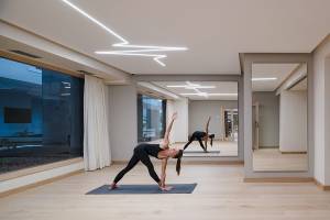 Yogaraum im Plus Fariones Suite Hotel mit zwei Frauen, die Yoga praktizieren, vor großen Fenstern.