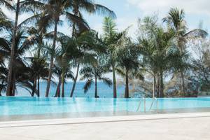 Ein Swimmingpool des Fariones Hotel mit Blick auf das Meer und Palmen im Hintergrund.