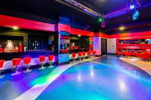 Innenbereich einer Hotelbar mit roten Stühlen, einer Theke und bunten Lichtern