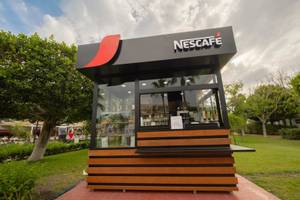 Außenansicht des Nescafé-Kiosks im Freien, umgeben von Bäumen und Rasen.