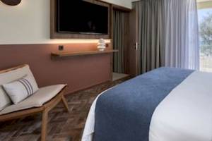 Hotelzimmer im Domes Aulus Zante mit Bett, Fernseher und Blick auf Bäume.
