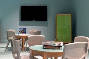 Spielzimmer im Domes Aulus Zante Hotel mit Tisch, Stühlen, Büchern und Fernseher.