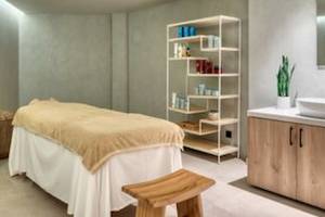 Massageraum im Domes Aulus Zante Hotel mit Massageliege, Regal, Waschbecken und Pflanze.