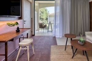 Innenansicht eines Zimmers im Domes Aulus Zante Hotel mit Wohnzimmer, Fernseher, Tisch und Stühlen.
