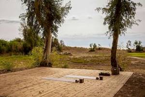 Yoga-Platz vor Bäumen im Freien mit zwei Matten, zwei Kerzen und einem Topf auf dem Boden.
