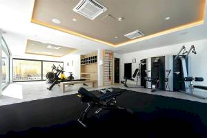 Fitnessbereich im H10 Costa Mogan Hotel mit verschiedenen Trainingsgeräten und einer Glaswand.