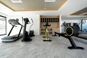 Fitnessbereich im H10 Costa Mogan Hotel mit mehreren Trainingsgeräten und einem Holzschrank.