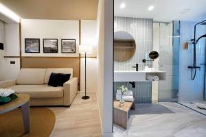 Innenansicht einer Suite im H10 Costa Mogan Hotel mit Wohnzimmer und Badezimmer.