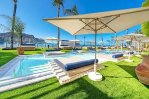 Pool-Loungebereich im H10 Costa Mogan Hotel mit Liegestühlen und Sonnenschirmen.