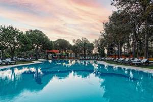 Am Abendaufnahme des Infinity-Pools im Megasaray Resort Side mit Sonnenliegen und Bäumen.