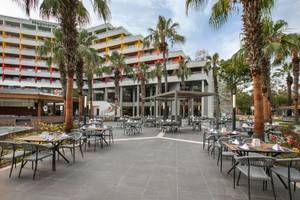 Außenbereich des Megasaray Resort Side mit mehreren Tischen und Stühlen unter Palmen.