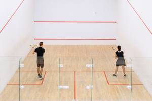 Zwei Spieler auf einem Squashplatz, einer mit Schläger, beide in Aktion.