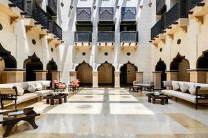 Lobby des Sharq Village und Spa, ein Ritz Carlton Hotel mit weißen Sofas und Tischen, Säulen und schwarzen Balkonen.