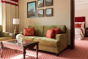 Suite-Wohnzimmer im Al Najada Doha Hotel by Tivoli mit grünem Sofa, rotem Kissen und kunstvollen Gemälden an der Wand.