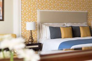 Hotelzimmer mit Bett, Blumen, Lampe und dekorativer Wandgestaltung.