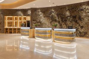 Empfangsbereich des Embassy Suites By Hilton Doha Old Town mit goldenen Rezeptionstresen und fischschuppenartiger Wandverkleidung.