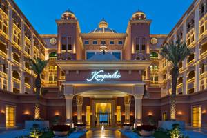 Der beleuchtete Eingang des Kempinski Marsa Malaz Hotels, The Pearl mit einem Brunnen und Palmen davor.