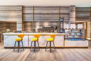 Barbereich im Rixos Gulf Hotel Doha mit Marmortheke und gelben Stühlen.