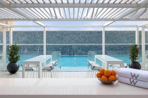 Pool im W Doha Hotel & Residences mit blauen Stühlen und Wasserfall.