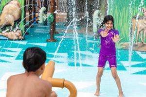 Ein Kind im Wasserpark des Waldorf Astoria Doha Lusail spielt mit Wasserfontaenen.