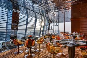 Innenansicht des Restaurants im Fairmont Doha mit modernen orangefarbenen Stühlen und Tischen vor großen Glaswänden.