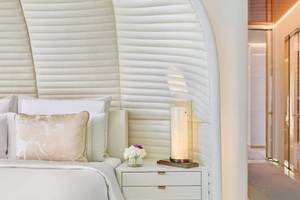 Schlafzimmer im Fairmont Doha Hotel mit weißen Möbeln, einem Bett, Kissen und einer Lampe auf dem Nachttisch.