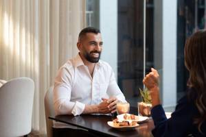 Ein Mann und eine Frau sitzen im Restaurant des Hyatt Regency Oryx Doha, lächeln und unterhalten sich.