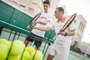 Zwei Männer auf dem Tennisplatz im Four Seasons Hotel Doha, einer hält eine Tennisschläger und der andere hält einen Ball.