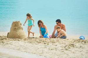 Eine Familie baut eine Sandburg am Strand, während das Meer im Hintergrund ist.