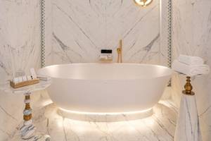 Badezimmer im Raffles Doha mit einer weißen Badewanne, Marmorwänden und goldenen Armaturen.