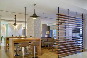 Innenbereich des Grand Park Lara Hotels mit Holzmöbeln, Barhockern, Couch und geometrischer Wandgestaltung.
