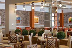 Innenansicht des Grand Park Lara Restaurants mit gedeckten Tischen, Sitzgruppen und dekorativen Pflanzen.