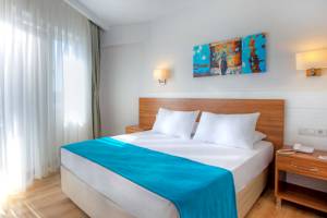 Schlafzimmer im Grand Park Lara Hotel mit blauer Bettdecke und weißen Kissen auf einem Bett mit Kopfteil.