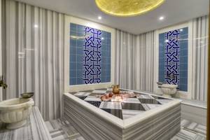 Innenansicht des Hamams im Grand Park Lara Hotel mit blauen und weißen Fliesen, Marmorbadewanne und zwei Waschbecken.