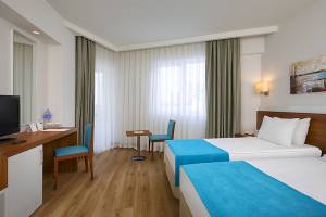 Innenansicht eines Doppelzimmers im Grand Park Lara Hotel mit zwei Betten, Schreibtisch und Fernseher.