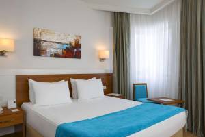 Schlafzimmer im Grand Park Lara Hotel mit einem Doppelbett, zwei weißen Kissen, blauer Decke, und einem blauen Stuhl neben einem Tisch.