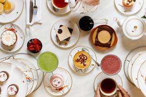 Luftaufnahme des Nachmittagstee-Angebots im St. Regis Doha mit verschiedenen Desserts, Getränken und Geschirr.