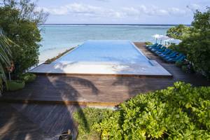 Infinity-Pool am Strand des Summer Island Maldives Hotels mit blauen Sonnenliegen und grünen Kissen.