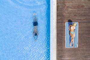 Blick von oben auf einen Pool im Hotel Summer Island Maldives mit einer Person, die schwimmt und einer anderen, die auf einem Handtuch liegt.